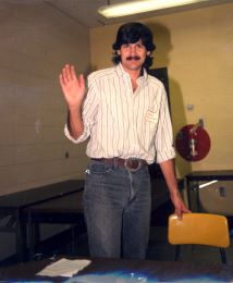 Ralph Holzenthal, 1980's - short black hair, mustache, white stiped shirt. Standing next to a desk. 