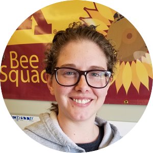 Jessica Helgen - short brown hair, glasses, grey sweatshirt, bee squad poster in the background 