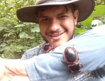 Dr Beza Beza, hearing a wide brimmed hat, long sleeve grey shirt, with 2 beetles on his arm